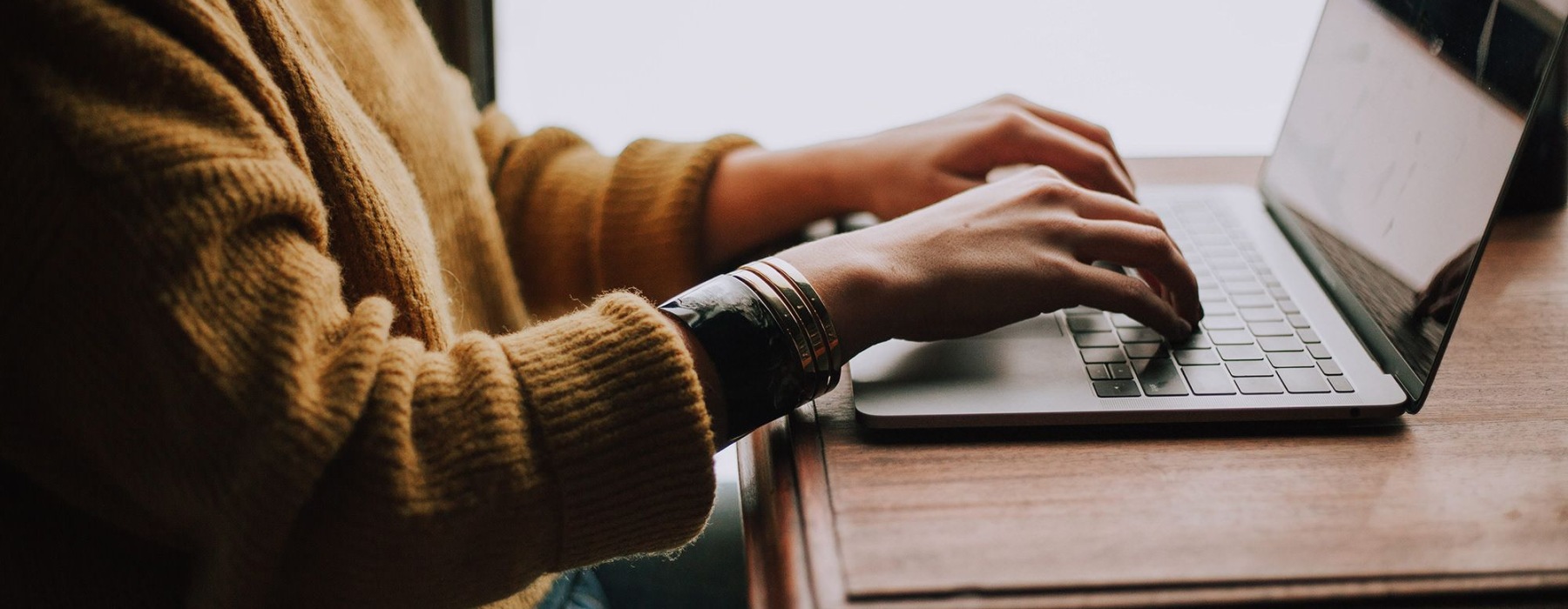 woman types on her laptop near large window